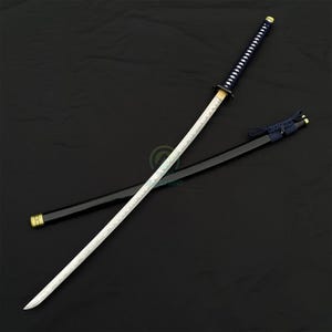 Może przedstawiać: Miecz katana z białym ostrzem i czarną rękojeścią. Rękojeść jest owinięta ciemnoniebieskim materiałem. Pochwa jest czarna ze złotymi akcentami. Miecz jest tradycyjną japońską bronią.