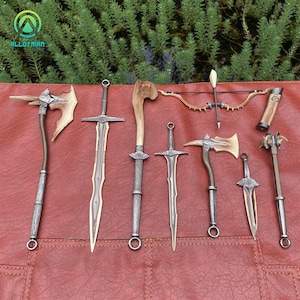 May include: An assortment of fantasy weapons, including swords, axes, a bow and arrow, and a mace, are displayed on a red surface. The weapons feature metallic and wooden elements, with intricate designs. The image showcases a variety of medieval-inspired weaponry.