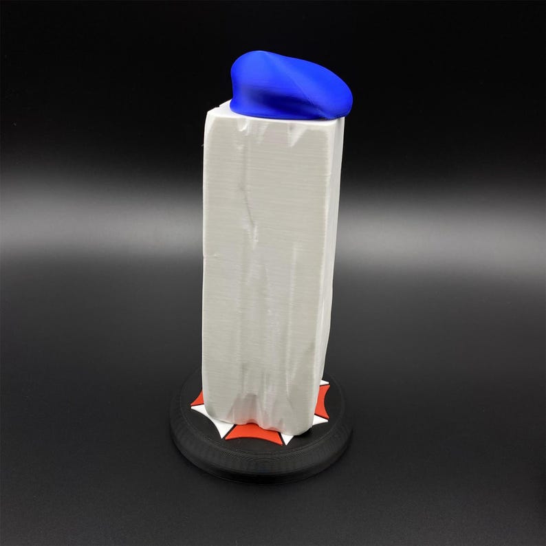 May include: A white rectangular object with a blue top, possibly a container or display item, sits on a black base with red and white accents. The object is on a black background.