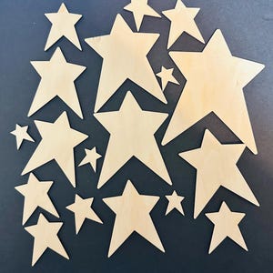 May include: A collection of wooden star cutouts in various sizes, arranged on a dark background. The stars are a natural wood color, with visible grain patterns. The arrangement includes both large and small stars, creating a celestial theme.