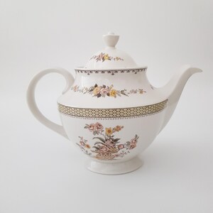 May include: White ceramic teapot with a floral pattern in shades of yellow, pink, and brown. The teapot has a lid and a spout.