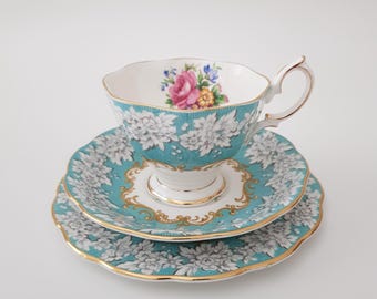 May include: A turquoise teacup and saucer set with a white floral pattern and gold trim. The cup features a pink and yellow floral design in the center.