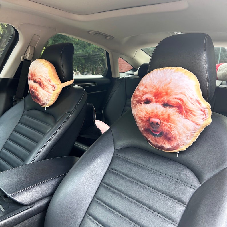 K&ouml;nnte beinhalten: Zwei Kopfst&uuml;tzen f&uuml;r Autos mit braunen und wei&szlig;en Kissen in Form von Hundek&ouml;pfen. Die Kissen sind aus weichem Stoff und haben ein realistisches Hundekopf-Motiv.