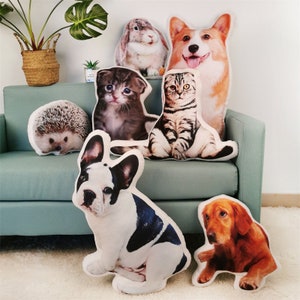 May include: A collection of plush animal pillows featuring a variety of animals, including a hedgehog, a cat, a dog, a rabbit, and a corgi. The pillows are all white with a realistic image of the animal printed on the front.