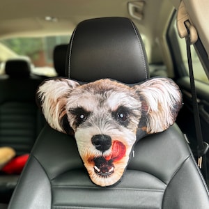 May include: A gray and white schnauzer dog head shaped car seat headrest. The dog has its tongue sticking out.