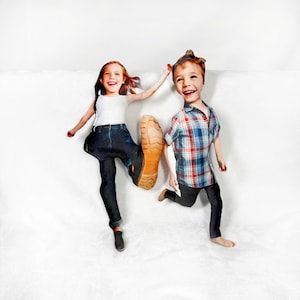 May include: A whimsical image features two children with oversized heads and cut-out bodies. One child kicks with a large boot, while the other runs. The girl wears a white tank top and jeans, the boy a plaid shirt and dark pants.