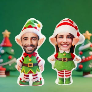 May include: Two Christmas elf-shaped plush dolls with smiling faces. The elves wear green and red outfits with striped socks and elf hats. The background is a solid green color, with Christmas trees in the background.