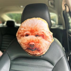 K&ouml;nnte beinhalten: Ein braunes und wei&szlig;es Kissen f&uuml;r die Kopfst&uuml;tze im Auto in Form eines Hundekopfes. Das Kissen ist aus weichem Stoff und hat ein realistisches Hundegesicht.
