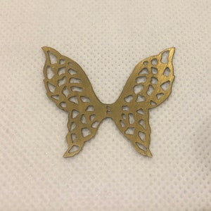 May include: A gold metal butterfly charm with a delicate, intricate design. The charm is cut out in the shape of a butterfly with wings that are detailed with a pattern of small circles and lines.