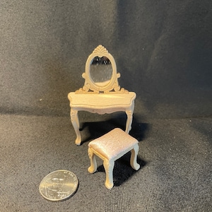 May include: A miniature vanity set with a white painted finish. The vanity has an oval mirror with ornate detailing and a small stool with a pink upholstered seat.