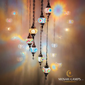 Może przedstawiać: 6-ramienna żyrandol z mozaikowego szkła z kolorowymi wzorami geometrycznymi. Żyrandol jest wykonany z metalu i ma zawieszenie łańcuchowe. Żyrandol ma szerokość 43 cm i wysokość 168 cm.  MULTICOLOR 1