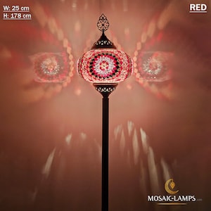 May include: A red mosaic glass floor lamp with a round shade and a decorative metal base. The lamp is 25 inches wide and 70 inches tall. The lamp is lit and casting a warm glow on the wall behind it.