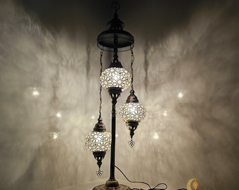 Puede incluir: Una lámpara de pie de tres luces con una base de metal negro y tres pantallas blancas en forma de globo con intrincados patrones geométricos. La lámpara tiene 34 cm de ancho y 107 cm de alto.  MEDIUM GLOBE.