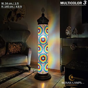 May include: A tall, colorful mosaic floor lamp with a black metal base. The lamp is 4.6 feet tall and 1 foot wide. The mosaic design features a variety of colors, including blue, green, yellow, and red. The lamp is lit and casting a warm glow on the surrounding area. The text "MULTICOLOR 3" is visible in the upper right corner of the image.