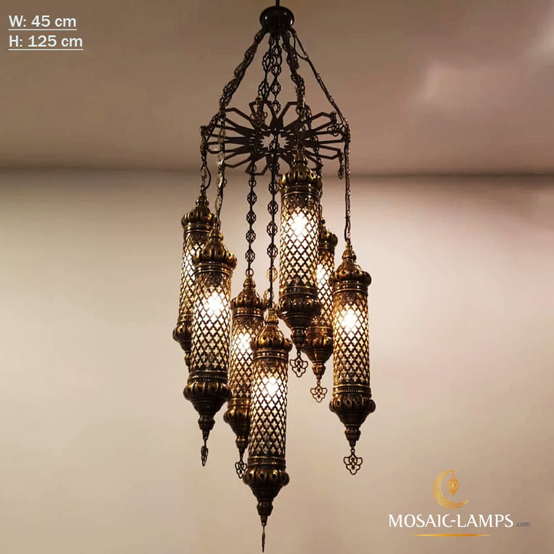 K&ouml;nnte beinhalten: Ein goldfarbener Kronleuchter mit mehreren h&auml;ngenden Lichtern. Der Kronleuchter ist aus Metall und hat ein geometrisches Design. Die Lichter sind in klarem Glas eingeschlossen und haben einen warmen Schein. Der Kronleuchter ist 45 cm breit und 125 cm hoch.