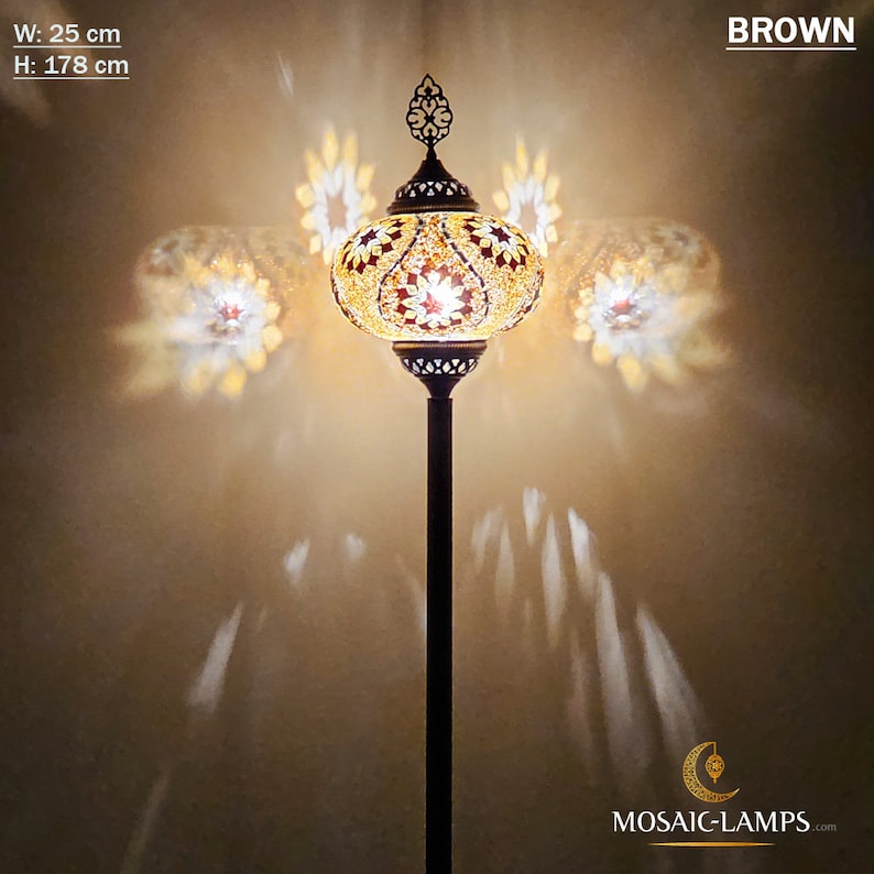 May include: A brown floor lamp with a mosaic glass shade. The shade is a round, globe shape with a gold and red pattern. The lamp is 25 inches wide and 70 inches tall. The lamp is lit and casting a warm glow on the wall behind it.