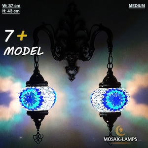 Op de afbeelding: Een zwarte metalen wandlamp met twee hangende mozaïekglazen lampen. De lampen zijn rond en hebben een blauw en wit mozaïekpatroon. De wandlamp is 37 cm breed en 43 cm hoog. 7+ MODEL