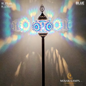 May include: A blue mosaic floor lamp with a round, patterned shade. The lamp is 25 inches wide and 70 inches tall. The lamp is lit and casting a colorful light pattern on the wall.