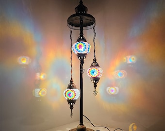 May include: A decorative floor lamp with three hanging mosaic glass lamps. The lamp is 42 inches tall and 13 inches wide. The lampshade is made of colorful glass pieces. The base and frame are dark bronze. The word "RAINBOW" is in the top right corner.