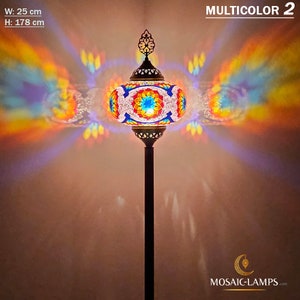 May include: A colorful mosaic glass floor lamp with a round shade and a black metal stand. The lamp is lit and casting a rainbow of colors on the wall. The lamp is 25 inches wide and 70 inches tall. MULTICOLOR 2