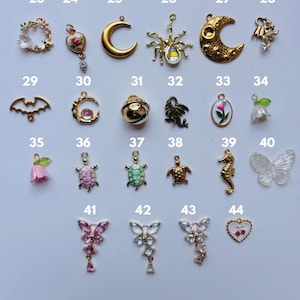Puede incluir: Una colecci&oacute;n de peque&ntilde;os dijes decorativos en varias formas, incluyendo lunas, flores, mariposas y animales. Los dijes son de oro, plata y colores pastel, algunos con piedras preciosas. La imagen est&aacute; tomada desde arriba.
