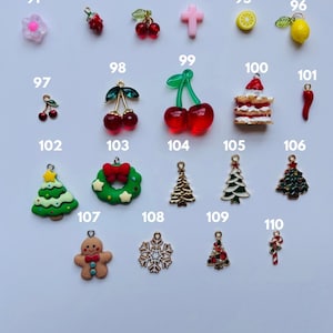 Puede incluir: Una colecci&oacute;n de abalorios coloridos, que incluyen una flor rosa, cerezas rojas, una cruz rosa, un lim&oacute;n, un pastel, un chile, un &aacute;rbol de Navidad, un hombre de jengibre y un copo de nieve. Para joyer&iacute;a o manualidades.