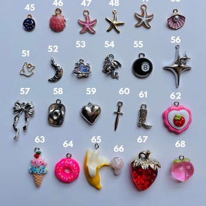 Puede incluir: Una colecci&oacute;n de peque&ntilde;os dijes de varias formas y colores. Incluye una luna creciente, un sombrero de vaquero, un coraz&oacute;n, una fresa, una rosquilla, un pl&aacute;tano, un hongo, una estrella, una concha y un lazo.