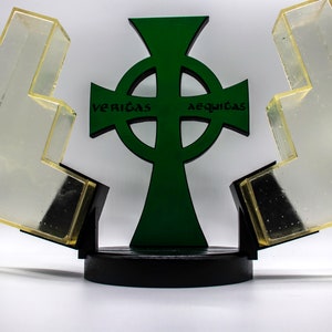May include: A green Celtic cross with the words "veritas" and "aequitas" inscribed on the arms. The cross is mounted on a black base and is surrounded by two clear acrylic pieces.