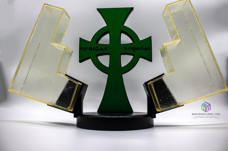 May include: A green Celtic cross with the words "veritas" and "aequitas" inscribed on the arms. The cross is mounted on a black base and is surrounded by two clear acrylic pieces.
