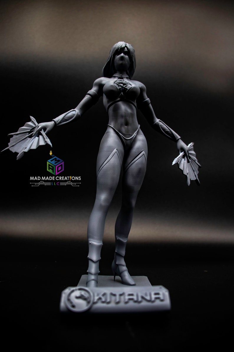 May include: A gray 3D printed figurine of a female character holding two fans. The figurine is standing on a base with the word "KITANA" printed on it.