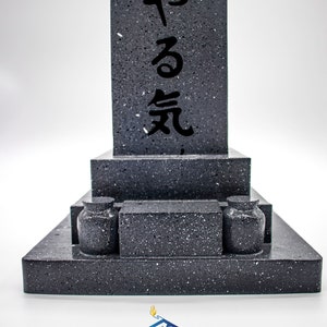 May include: A black granite Japanese style grave marker with the inscription "やる気" in black lettering. The marker is made up of three tiers with two small black urns on the bottom tier.