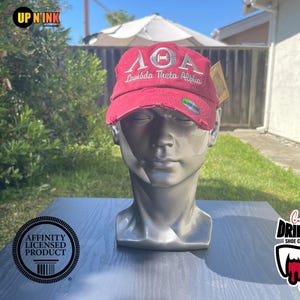 May include: A red distressed baseball cap with a white embroidered logo that says "ΛΟΑ Lambda Theta Alpha".