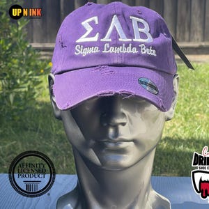 May include: A purple distressed baseball cap with white embroidery that reads "ΣΛΒ Sigma Lambda Beta".