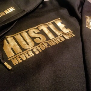 May include: Black hoodie with gold lettering that reads "Hustle Never Stop, Never Quit" and a smaller gold logo that reads "Pure Paper Prodigy" on the sleeve.