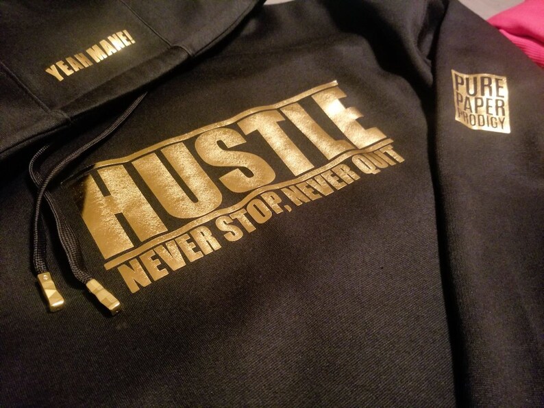 May include: Black hoodie with gold lettering that reads "Hustle Never Stop, Never Quit" and a smaller gold logo that reads "Pure Paper Prodigy" on the sleeve.