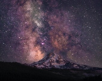 May include: A night scene showing a mountain with snow under a starry sky. The Milky Way is visible, with colours of purple, pink, and orange. A dark forest and a lake are in the foreground of the image.