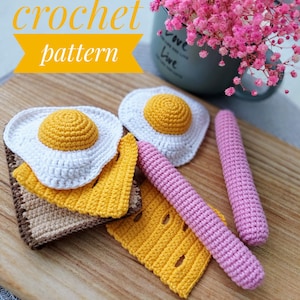 May include: Crochet pattern for a breakfast food set, including two fried eggs, two slices of cheese, and two sausage links. The eggs are white with yellow yolks, the cheese is yellow, and the sausage links are pink.