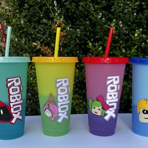 May include: Four colorful reusable cups with lids and straws. Each cup features a different Roblox character and the word "Roblox" printed on the side.