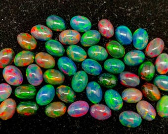 Puede incluir: Una colección de ópalos ovalados con colores vibrantes, incluyendo verde, azul, rojo y naranja. Los ópalos se exhiben sobre una superficie negra, mostrando sus cualidades iridiscentes. Estas piedras preciosas son ideales para la creación de joyas.