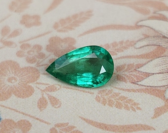 May include: A pear-shaped emerald gemstone with a deep green color. The gemstone is faceted and has a high degree of brilliance.