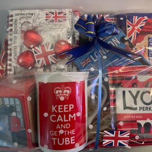 May include: A gift basket with a red and white mug that says "Keep Calm and Get the Tube". The basket also includes a box of chocolates, a bag of coffee, and a blue ribbon.