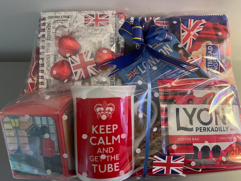 May include: A gift basket with a red and white mug that says "Keep Calm and Get the Tube". The basket also includes a box of chocolates, a bag of coffee, and a blue ribbon.