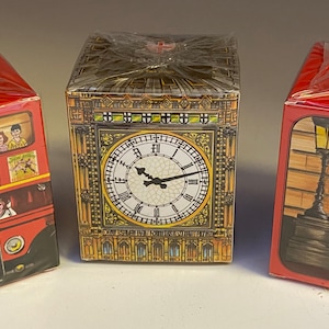 May include: Three red boxes with different images of London landmarks. The first box features a red double-decker bus with the text "Tower of London, Trafalgar Square, 15". The second box features Big Ben with a clock face. The third box features a red telephone booth and a guard in a red uniform.