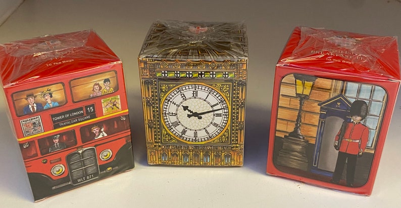 May include: Three red boxes with different images of London landmarks. The first box features a red double-decker bus with the text "Tower of London, Trafalgar Square, 15". The second box features Big Ben with a clock face. The third box features a red telephone booth and a guard in a red uniform.