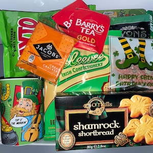 May include: A St. Patrick's Day gift basket with a green mug featuring a cartoon leprechaun, a bag of Jacobs Cream Crackers, a bag of Barry's Gold Tea, a bag of Reeves Irish Confectionery, a bag of O'Neill's Shamrock Shortbread, and a bag of green and gold candy.