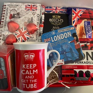 May include: A red and white gift basket with a mug that says "Keep Calm and Get the Tube" and other London themed items, including a notebook, chocolate, shortbread, and tea.