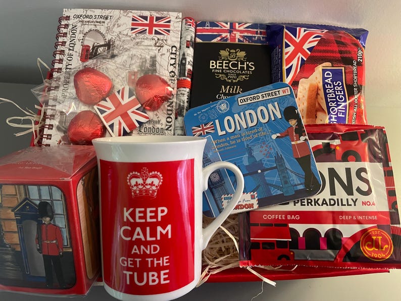 May include: A red and white gift basket with a mug that says "Keep Calm and Get the Tube" and other London themed items, including a notebook, chocolate, shortbread, and tea.