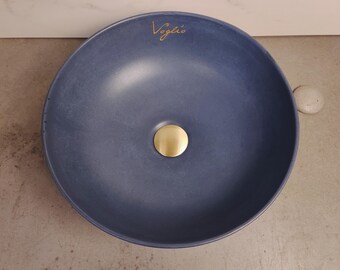 May include: A round, dark blue ceramic sink with a gold drain stopper. The sink has the word "Voglio" written on the top.