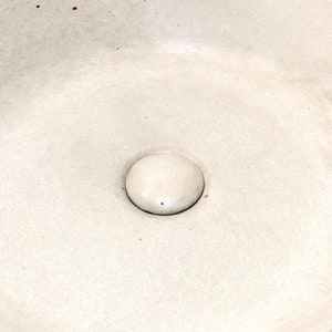 Puede incluir: Un lavabo de cerámica blanca con un agujero de drenaje redondo y la palabra "Voglia" escrita en letras doradas.