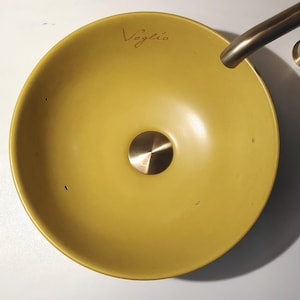Peut inclure: Un lavabo de salle de bain en céramique jaune avec un bouchon de vidange en or. Le lavabo porte l'inscription "Voglie" à l'intérieur.